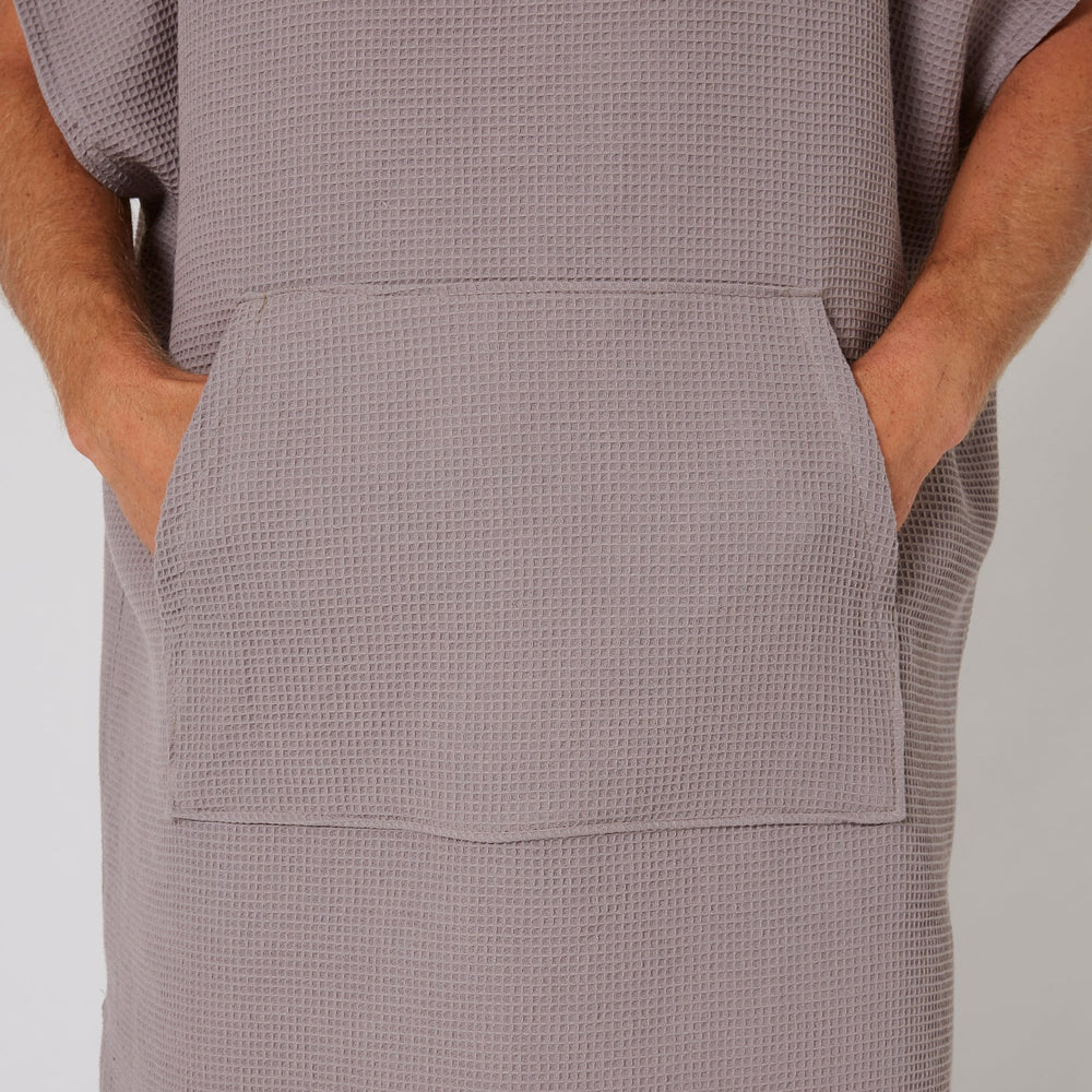 Person wearing a textured gray dress with pockets on a plain background