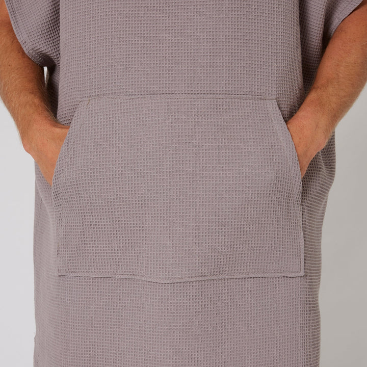 Person wearing a textured gray dress with pockets on a plain background