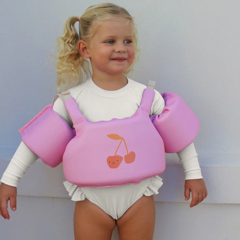 Child wearing a pink life jacket with cherry design against a plain background
